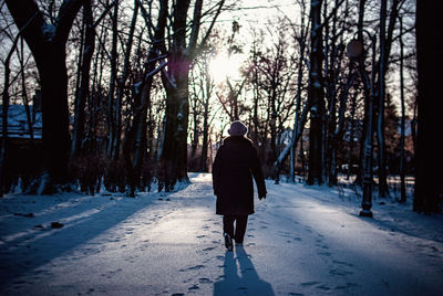 Rear view of person walking on snowy field against bare trees