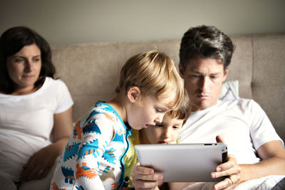 Woman looking at man using tablet computer with children on bed at home