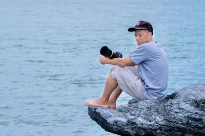 Side view of young man sitting on rock by sea