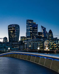 Illuminated buildings by river against blue sky