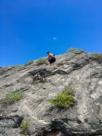 Low angle view of man rock climbing against blue sky