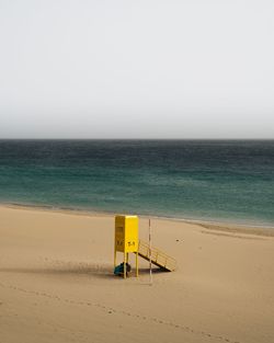 Children sitting by lifeguard hut at beach against clear sky