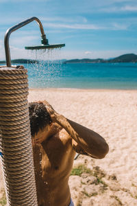 Shirtless man taking shower at beach against sky