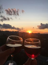 Close-up of hand holding beer glass against sky during sunset