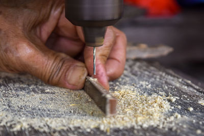 Cropped hands of craftsperson drilling on wood at workshop