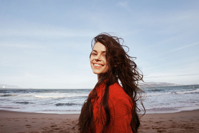 Young woman standing at beach against sky