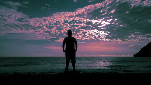 Rear view of silhouette man standing at beach during sunset