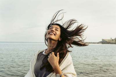 Young woman smiling while looking at sea against sky