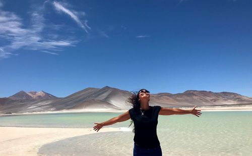 Woman with arms outstretched standing at beach against blue sky