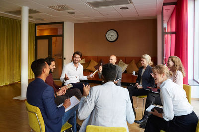 Smiling entrepreneurs discussing while sitting in circle during office workshop