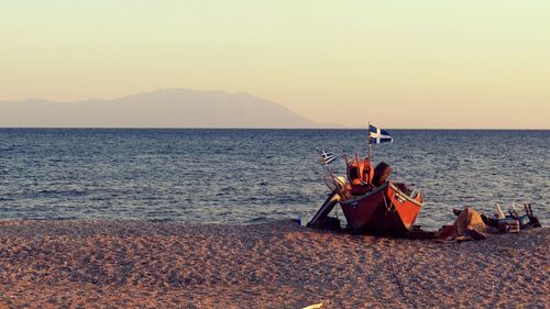 Boat moored on shore by sea against clear sky during sunset