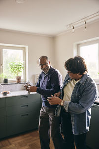 Playful senior couple dancing with each other while standing in kitchen at home