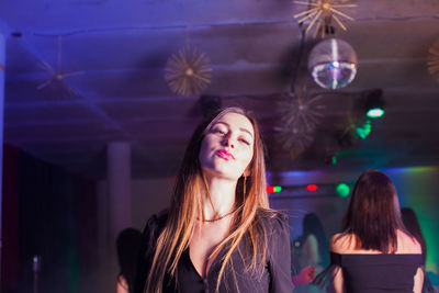 Portrait of young woman standing against illuminated nightclub