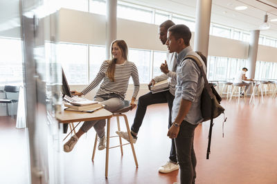 Friends looking at woman using computer at desk in university cafeteria