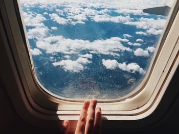 Cropped image of hand by airplane window against sky