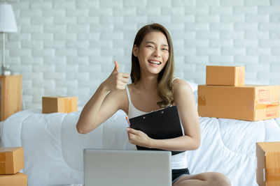 Portrait of woman gesturing while sitting amidst cardboard boxes at home