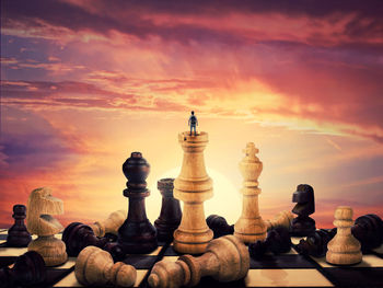 Boy stand on a chess piece meet the sunrise on the horizon. gigant figures scattered on chessboard