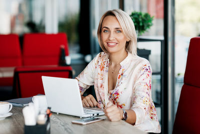 Smiling young woman using phone while sitting on table