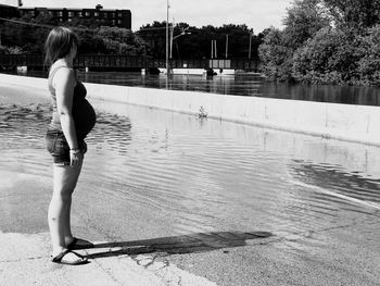 Side view of pregnant woman standing by lake on sunny day