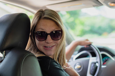 Portrait of smiling young woman wearing sunglasses in car