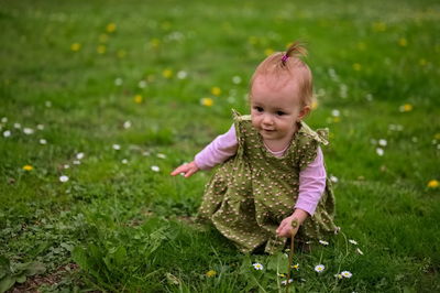 A little girl is crouching in the grass and picking flowers