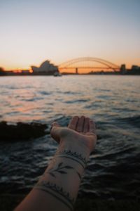 Hand on bridge over sea against sky during sunset