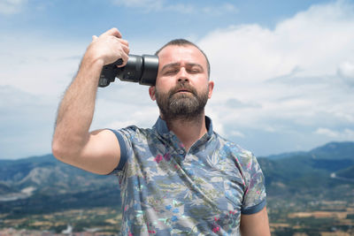 Portrait of man holding camera against sky