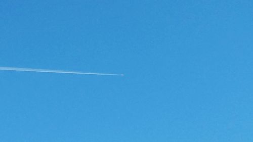 Low angle view of vapor trails against clear blue sky