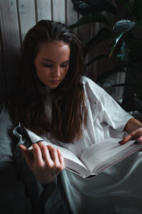 Young woman reading book while sitting at home