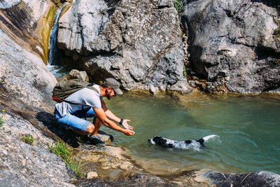 Male owner of spaniel dog walking against mountains and waterfall background.