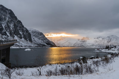 Scenic view of frozen lake by snowcapped mountains against sky during sunset