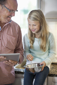 Grandfather and granddaughter using digital tablet while cooking in kitchen
