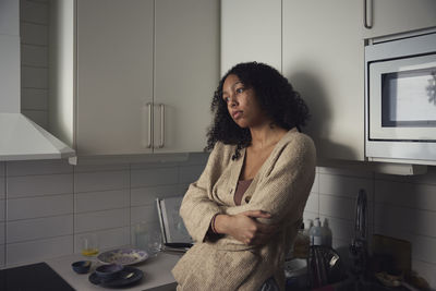 Pensive young woman standing in kitchen