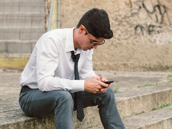Man wearing tie using phone while sitting on steps