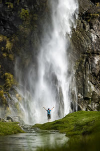 Figure standing in front of waterfall spray, in green nature landscape