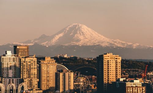 Buildings by snowcapped mountain against sky during sunset