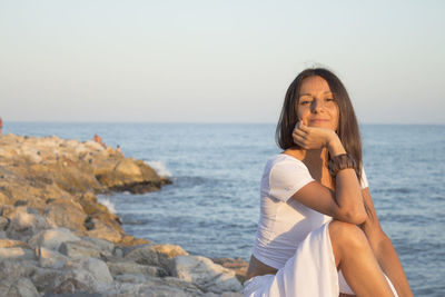 Portrait of woman sitting on rock against sea
