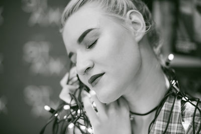 Close-up of young woman with eyes closed holding illuminated string lights at home