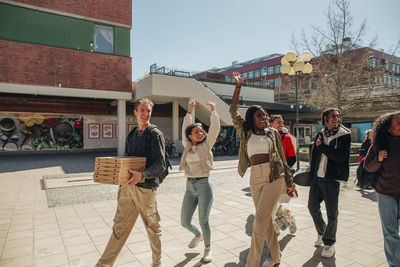 Happy multiracial friends waving hands while walking at street on sunny day