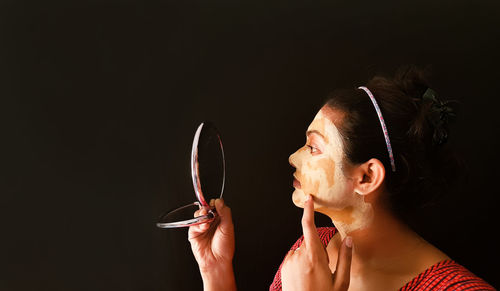 Portrait of woman holding eyeglasses against black background