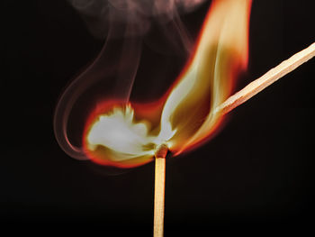 Close-up of burning matchstick against black background