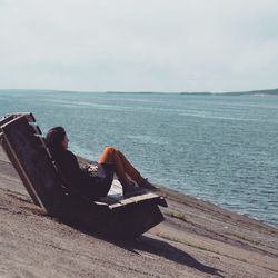 Man sitting on wood by sea against sky