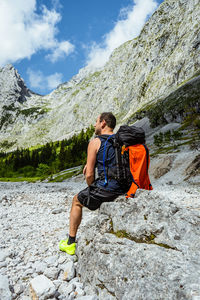 Rear view of man with backpack sitting on rock