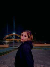 Portrait of young woman standing against sky at night