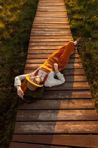 Woman naturalist resting lying on backpack on wooden path through peat bog swamp in national park