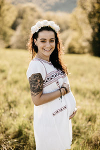 Portrait of smiling pregnant woman standing on field