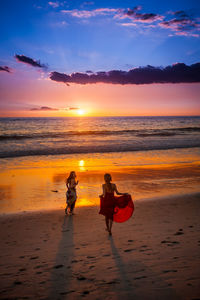 Silhouette people on beach against sky during sunset