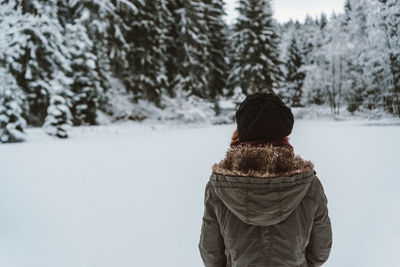 Rear view of woman standing against trees during winter