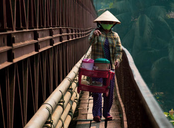 Woman wearing hat carrying containers while walking on footbridge