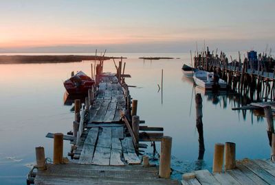 Fishing boats moored at sea against sky during sunset